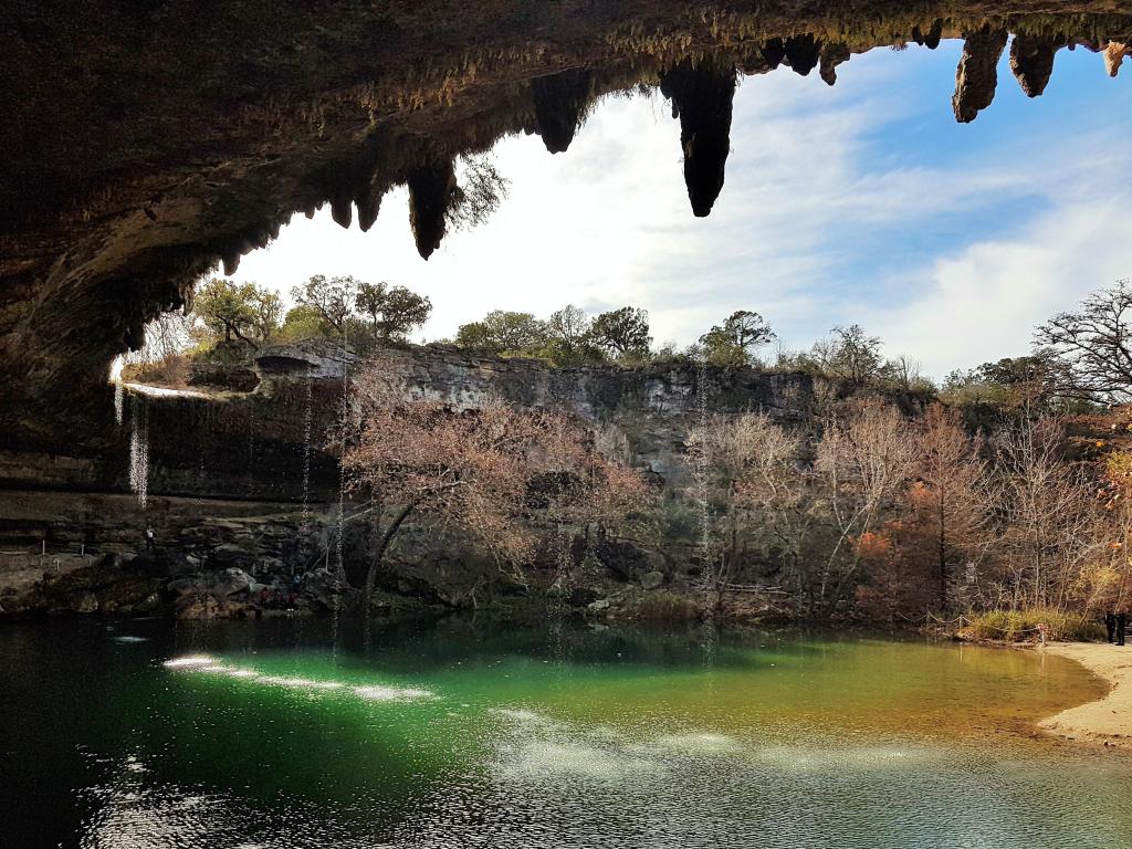 Hamilton Pool Preserve, Texas, USA taken from inside the cave looking at the bright green waters of the pool and surrounded by trees.