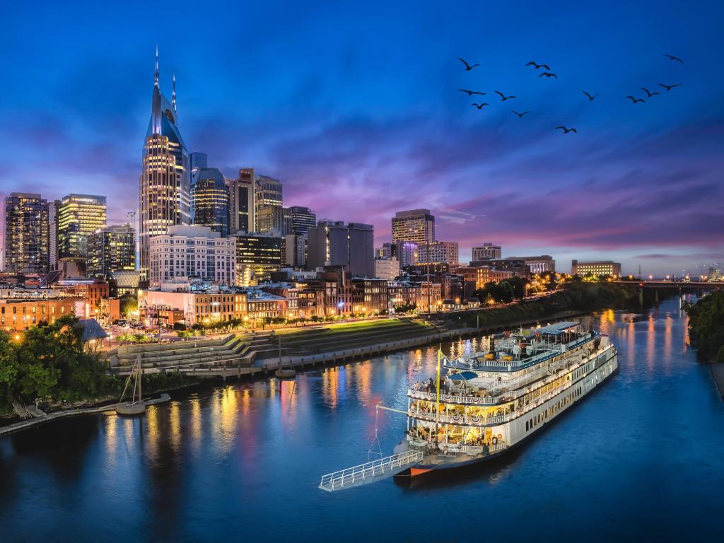 Nashville skyline at night, with a boat passing by on the river in the foreground