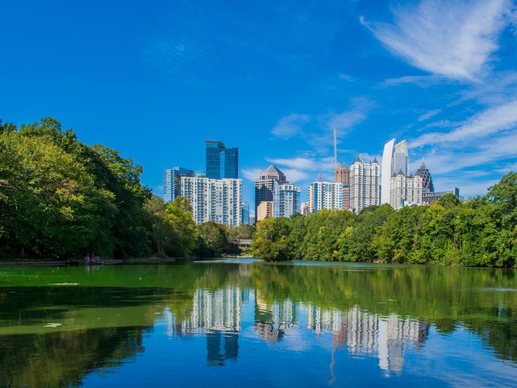 Atlanta, Georgia, USA with the city skyline in the background on a summer afternoon and trees lining the lake in the foreground.