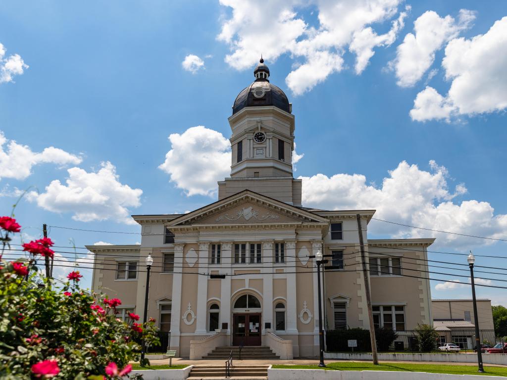 View of historic Claiborne County Courthouse in Port Gibson, Mississippi on a sunny day with red flowers in the foreground