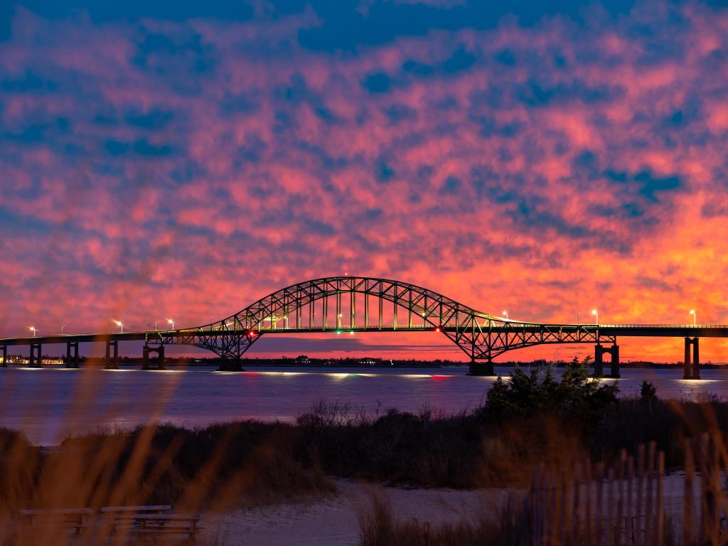 Vibrant colorful sunset with pinks and purples, sky behind a long steel tied arch bridge