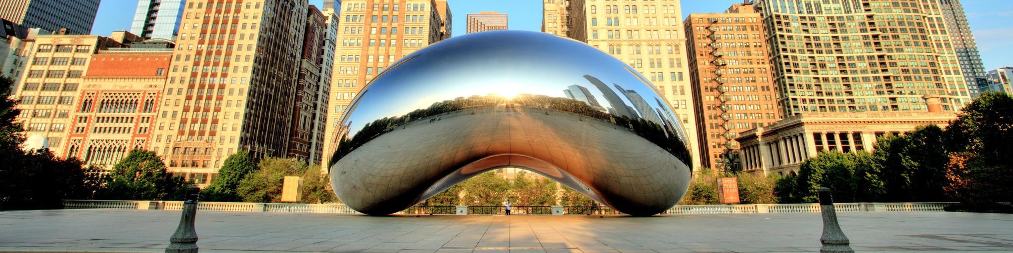 View of the famous metal sculpture in Chicago with tall buildings in the background with blue sky
