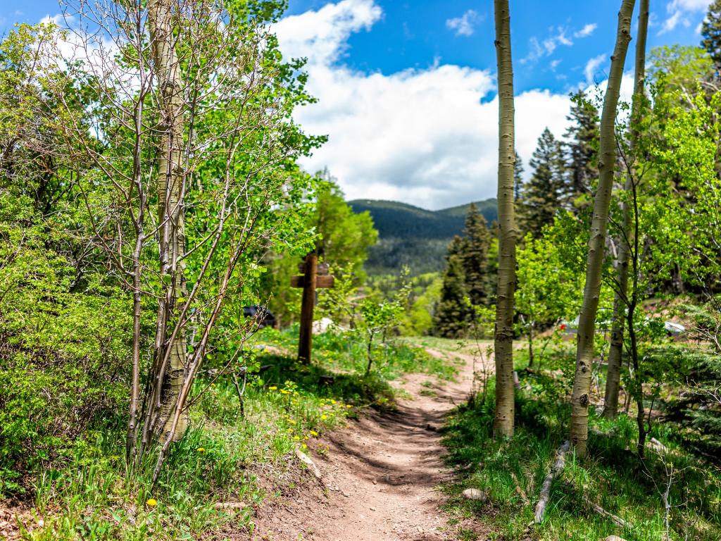 Santa Fe National Forest park trail with sign entrance at trailhead Sangre de Cristo mountains and green aspen trees by parking lot.