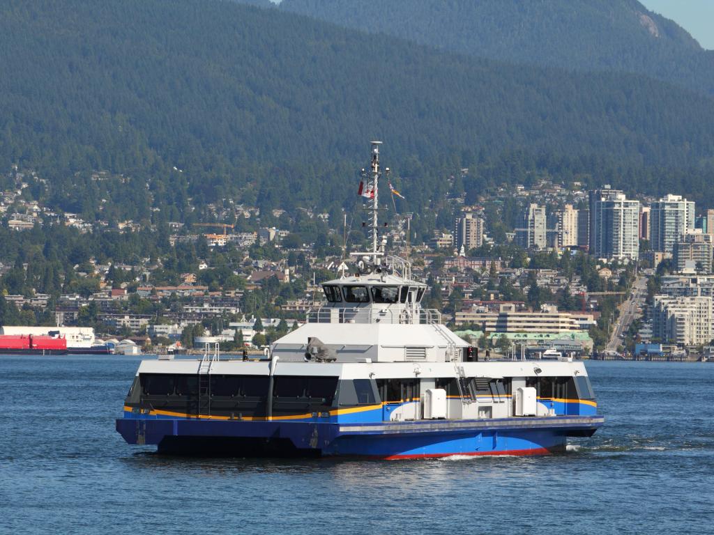 A commuter ferry crosses Vancouver's Burrard Inlet from North Vancouver, city and forested hills in the background