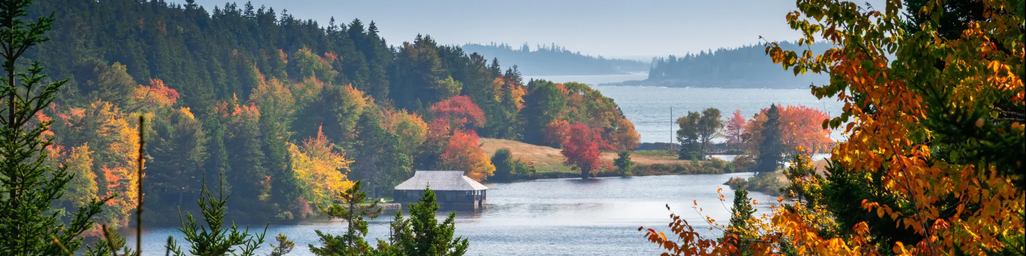 The ocean as seen through fall foliage at Acadia National Park in Maine, with a wooden hut on a jetty 