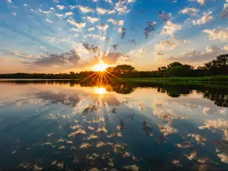 Sunset over water near Omaha, Nebraska with rays of light shimmering on the clouds and water