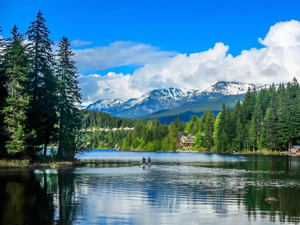 Whistler, British Columbia, Canada with a view of the Alta Lake in the foreground and trees lining the shore with snow-capped mountains in the distance on a sunny day.