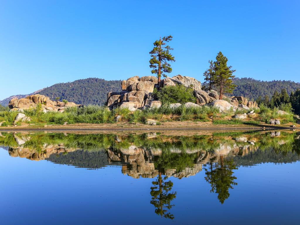 Boulder Bay, Big Bear Lake, California, USA taken on a bright blue sunny day with the lake in the foreground and the boulders and trees in the background reflecting in the waters edge. 