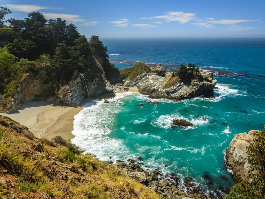 Turquoise waters at Mcway Falls beach waterfall on the Big Sur Coast of California, under a blue sky