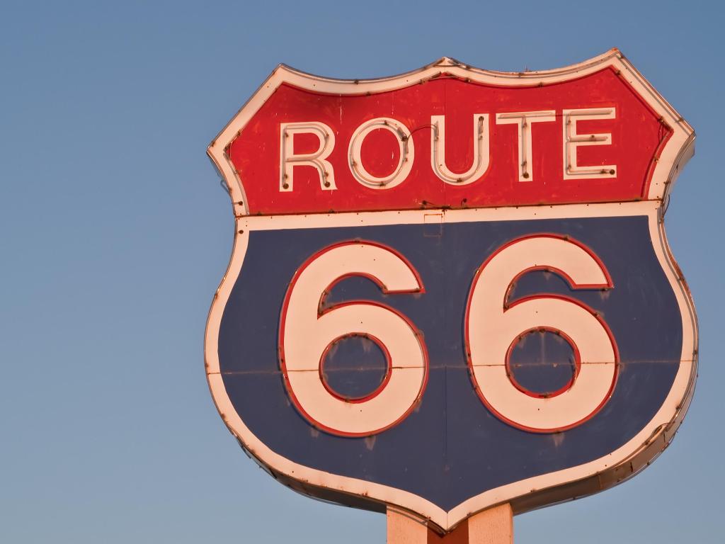 Red, white, and blue Route 66 neon sign in the shape of a US Highway shield glowing without the neon at sunset