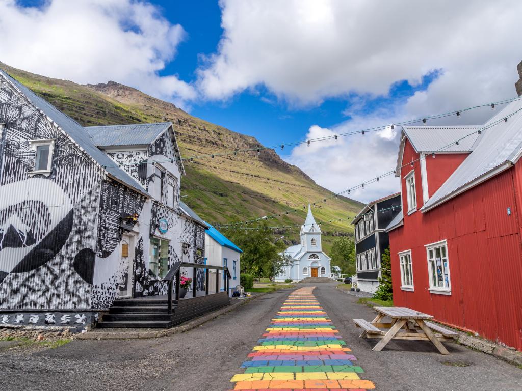 Colorful buildings line a rainbow path that leads to a chapel in Seyðisfjörður, Iceland. Image taken on a summer day 