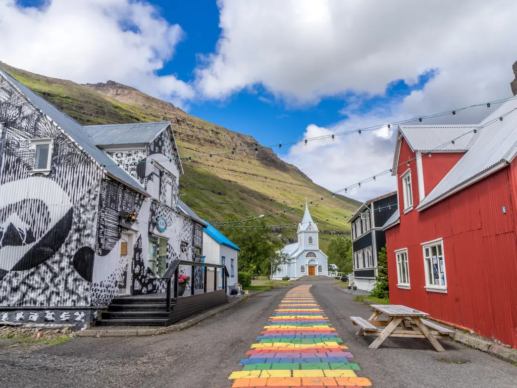 Colorful buildings line a rainbow path that leads to a chapel in Seyðisfjörður, Iceland. Image taken on a summer day 
