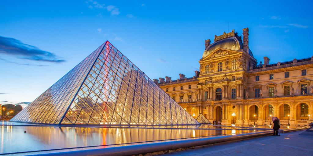 The glass pyramid of The Louvre museum, Paris, with its intricate old buildings in the background, at sunset