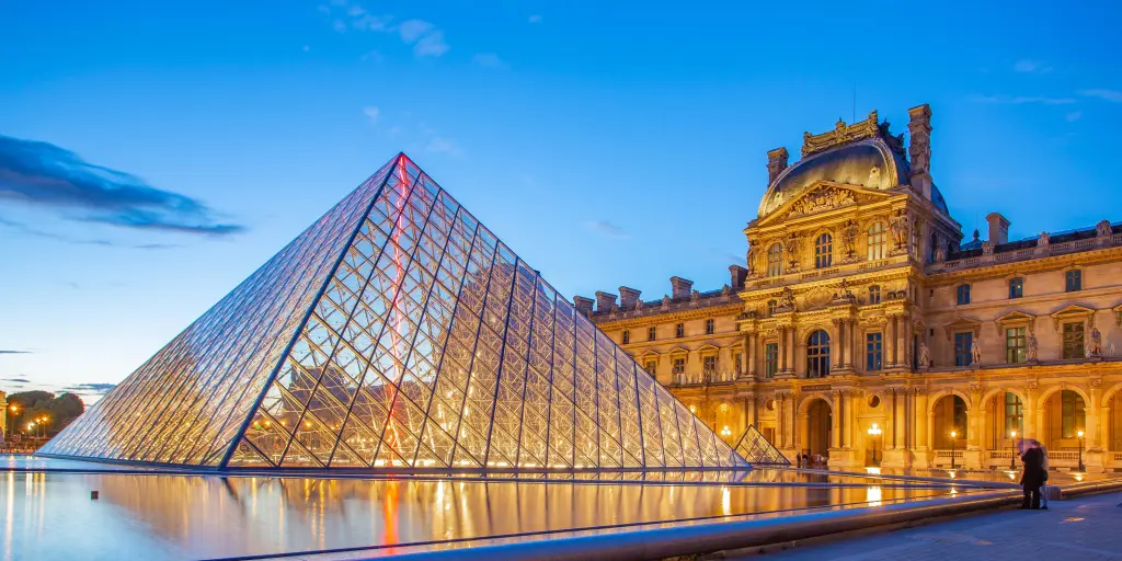 The glass pyramid of The Louvre museum, Paris, with its intricate old buildings in the background, at sunset