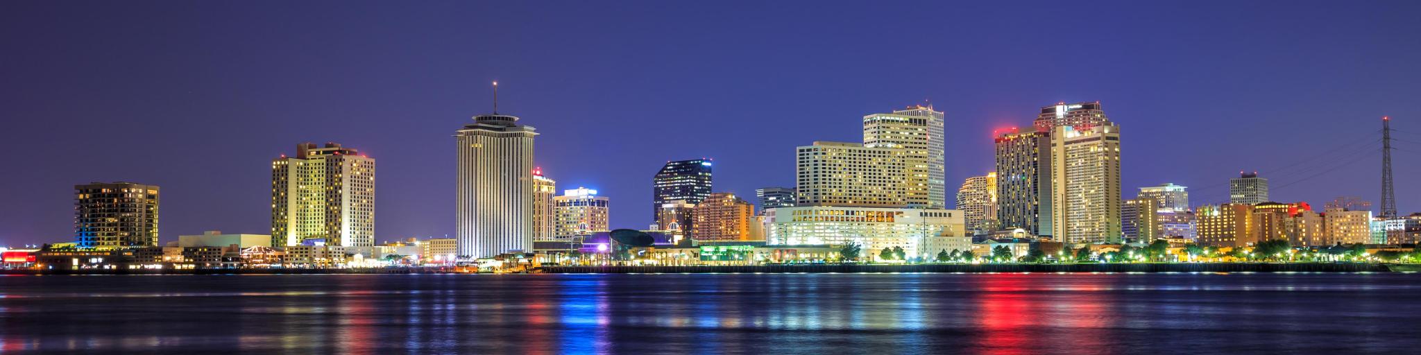 New Orleans, Louisiana, USA with the city downtown in the background and the Mississippi River in the foreground at twilight.