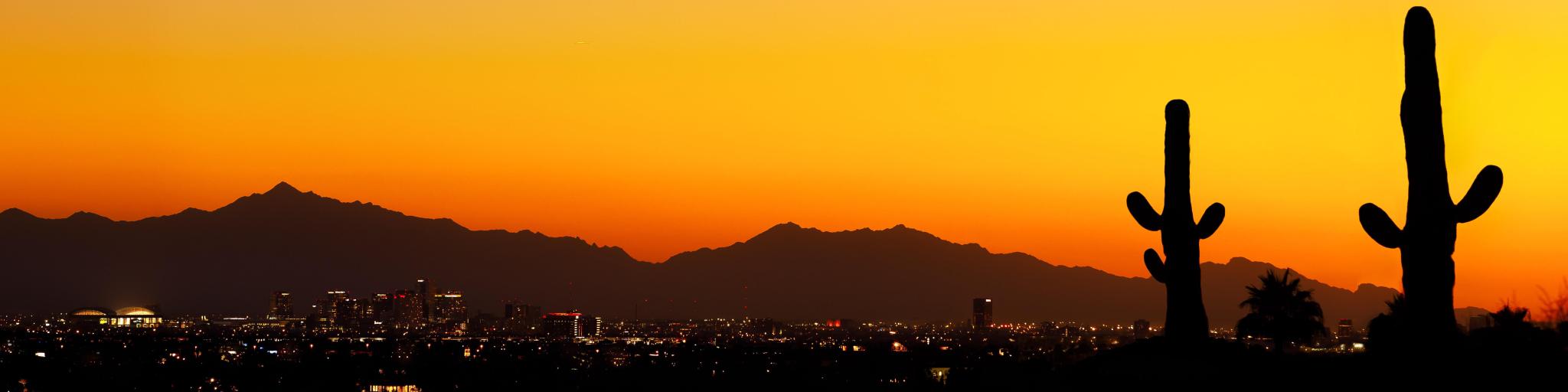 Silhouette of mountains with vibrant orange sky and outline of buildings in shadow in the foreground