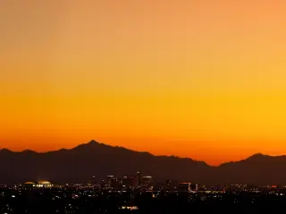 Silhouette of mountains with vibrant orange sky and outline of buildings in shadow in the foreground
