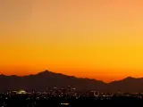 Silhouette of mountains with vibrant orange sky and outline of buildings in shadow in the foreground