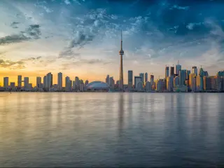 Toronto skyline, Canada taken at sunset with calm waters in the foreground and the city skyline in the distance.