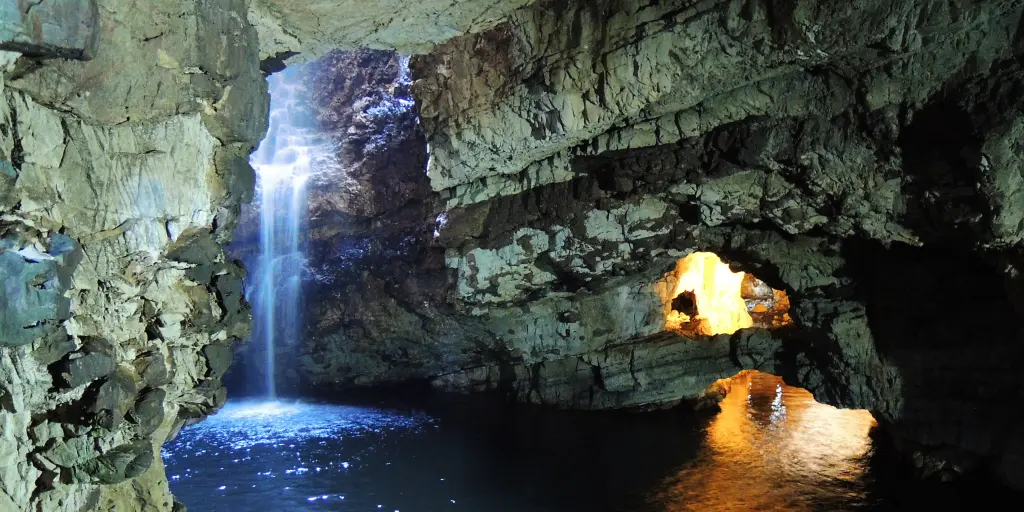 A waterfall falls inside Smoo Cave, Scotland, with light shining through from above