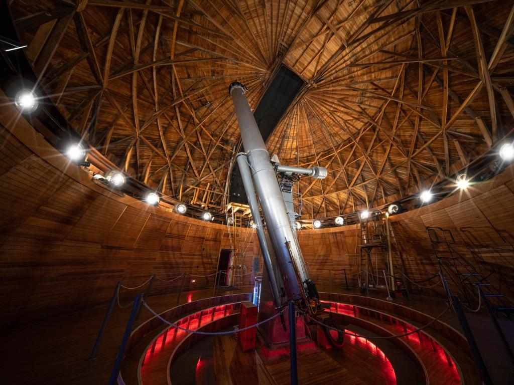 Inside Lowell Observatory of Flagstaff, with large telescope in centre and bright red lighting marking walkway