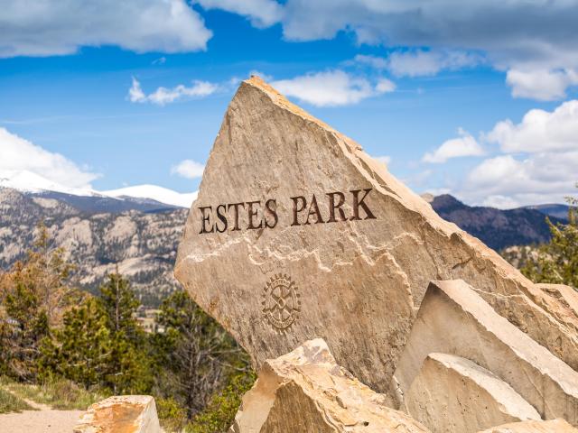 Estes Park sign etched onto large rock, surrounded by mountains and blue skies