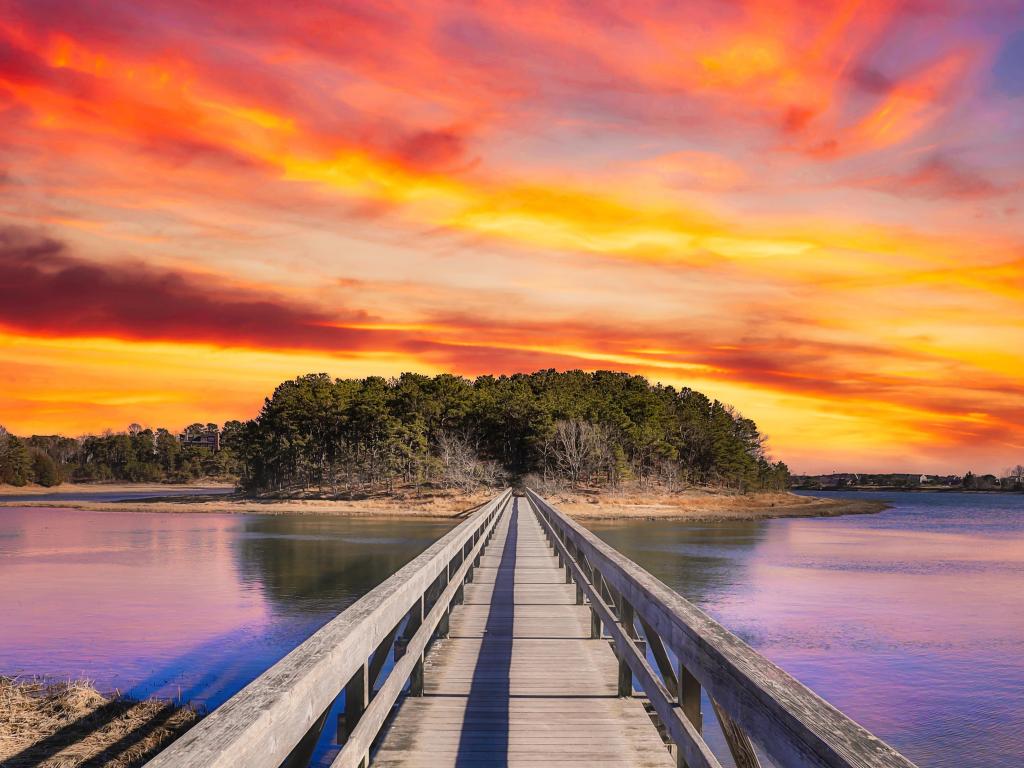 Wooden bridge across lagoon to small island with vibrant sunset