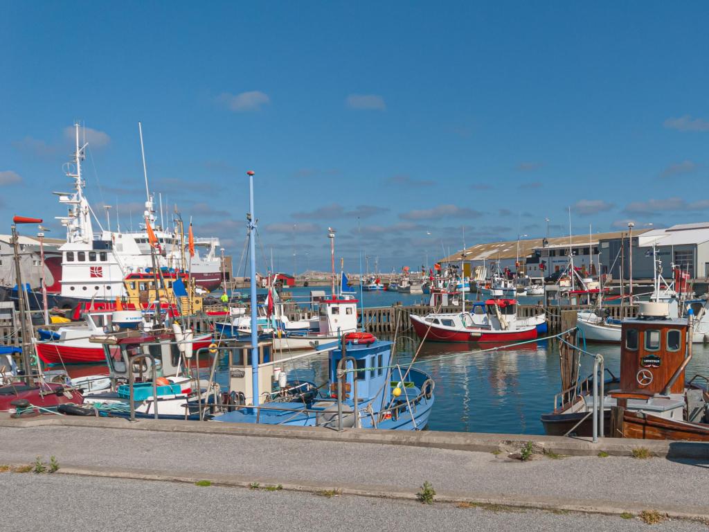 Fishing boats line the docks at Hirtshals Port, Denmark, on a clear summer's day with calm waters and a blue sky above