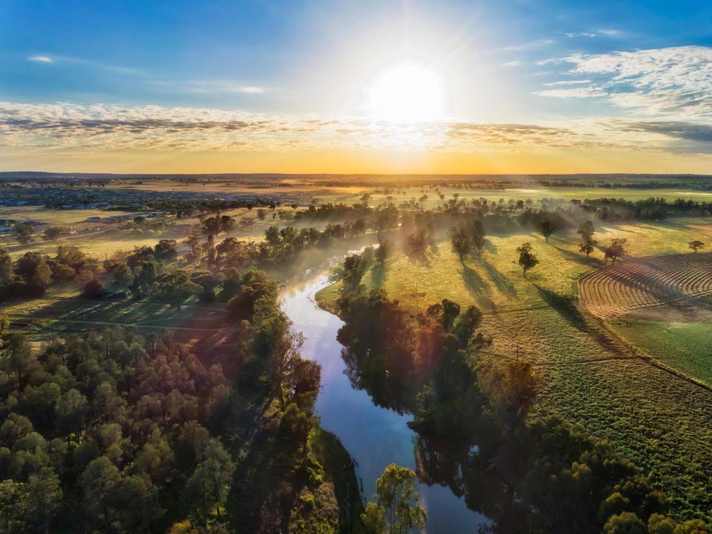 Macquarie River, Dubbo in the centre with farm fields either side and taken as an aerial shot with the sun rising in the distance. 