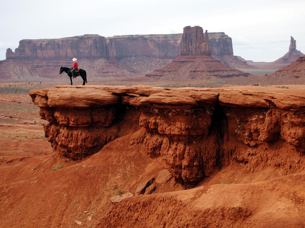 Man with white cowboy hat riding a black horse overlooking John Ford's Point and canyons