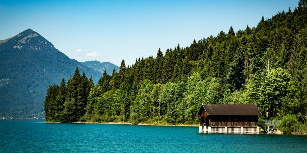 A little alpine hut on a jetty above very blue water in Walchensee Lake, Bavaria, Germany, with pine trees and mountains in the background