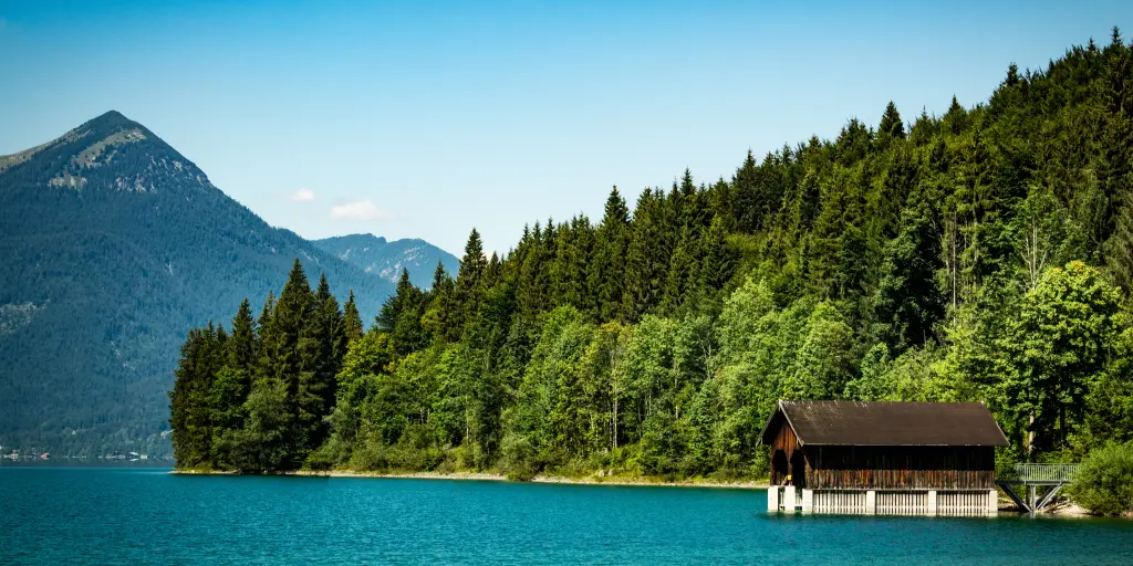 A little alpine hut on a jetty above very blue water in Walchensee Lake, Bavaria, Germany, with pine trees and mountains in the background