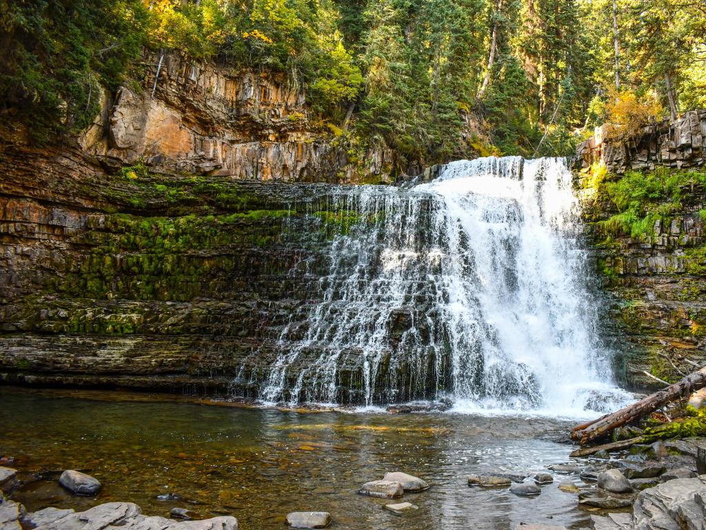 Ousel Falls Waterfall, Big Sky, Montana, USA with rocks and trees in the distance and calm water in the foreground. 