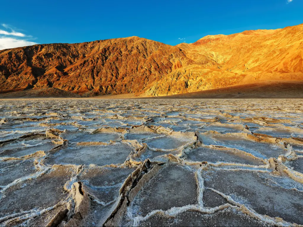 Badwater basin at sunset, Death Valley National Park, California with dry soil and mountains in the background.