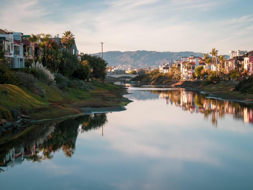 Grand Canal in Marina Del Ray, California, USA taken at sunset with the water in the foreground, houses and grass either side and hills in the distance. 