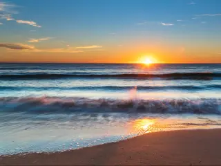 Vibrant sunrise light illuminating calm water breaking on a beach