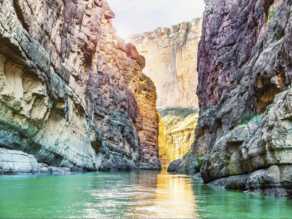 High canyon cliffs with turquoise river running between them and golden light illuminating the rocks and water in places