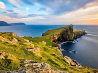 Isle of Skye, UK with a view of Neist Point Lighthouse in the distance bathed in golden light from the setting sun.