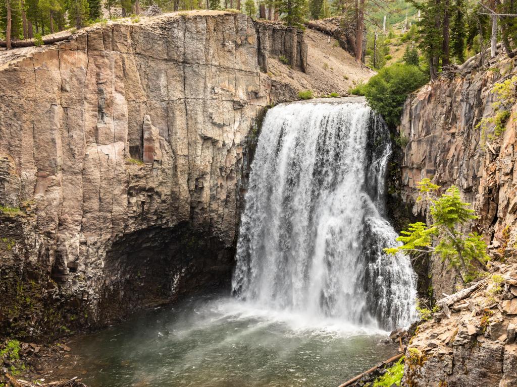 Rainbow Falls in Devils Postpile National Monument, California with cliffs either side of the waterfall and some greenery surrounding.