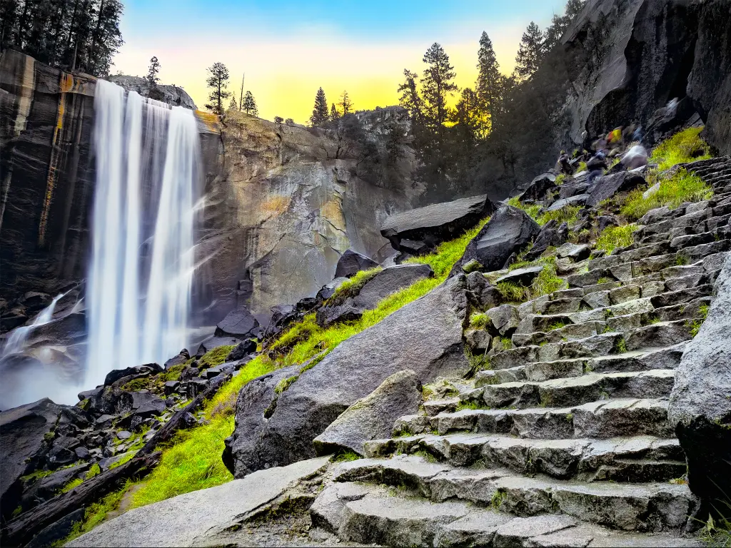 The image shows the Vernal Falls on the left and its staircase trail on the right side at dawn.