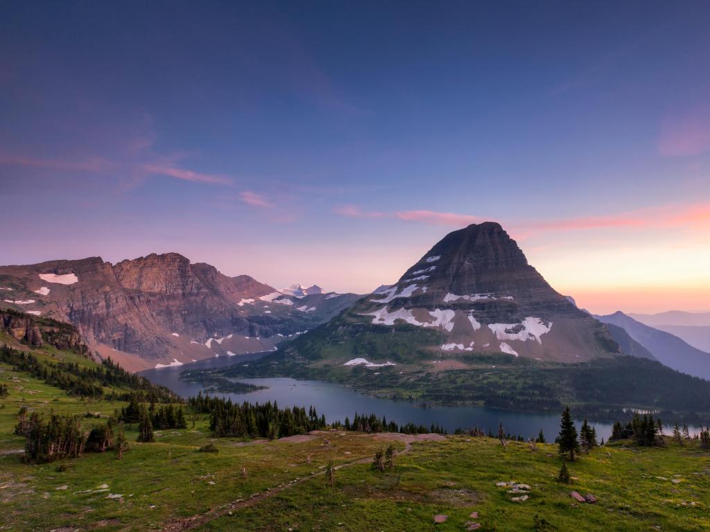 Glacier National Park, Montana, USA taken at Hidden Lake Trail, Logan Pass at sunset with grass in the foreground and snow-covered mountains in the distance. 