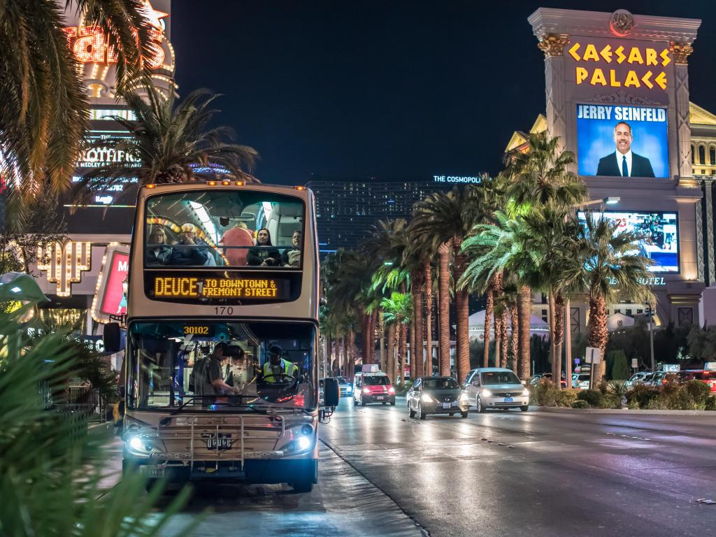 Famous bus that runs up and down Las Vegas Boulevard at night with Caesars Palace in the background