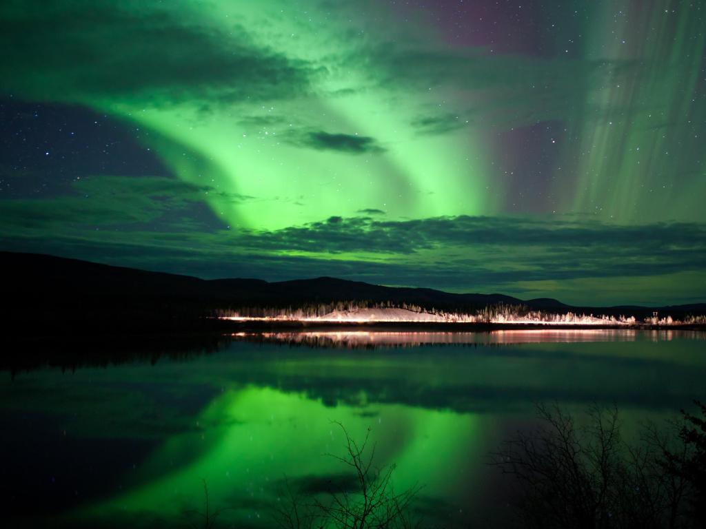 Night Sky Stars, clouds and Northern Lights over country road at lake shore