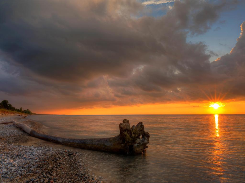 Driftwood on a sandy beach by Lake Huron with vivid orange sunset and cloudy sky