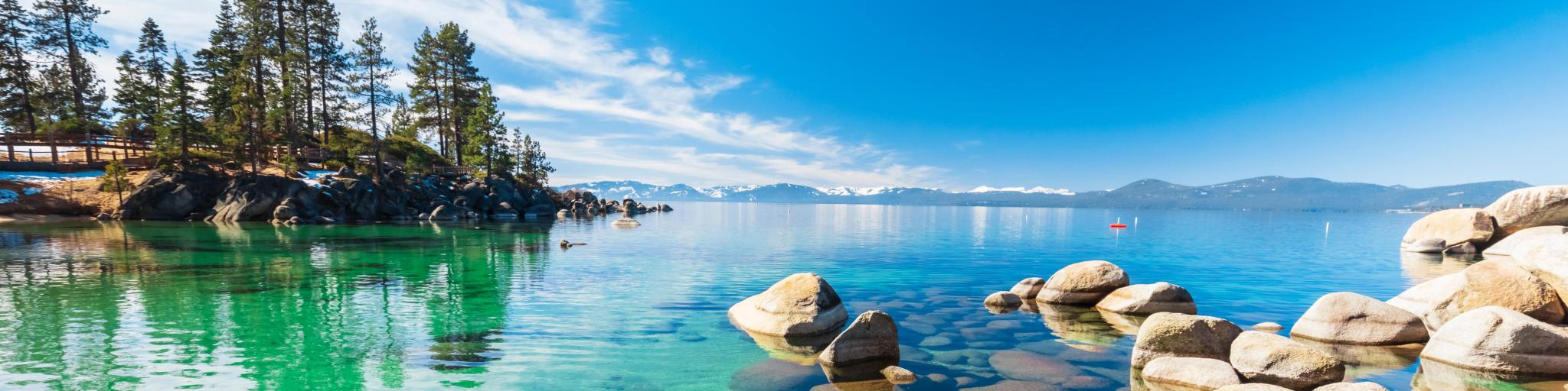 Clear turquoise water, rocky shoreline in sunny day, beach with blue sky over clear transparent water