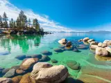 Clear turquoise water, rocky shoreline in sunny day, beach with blue sky over clear transparent water
