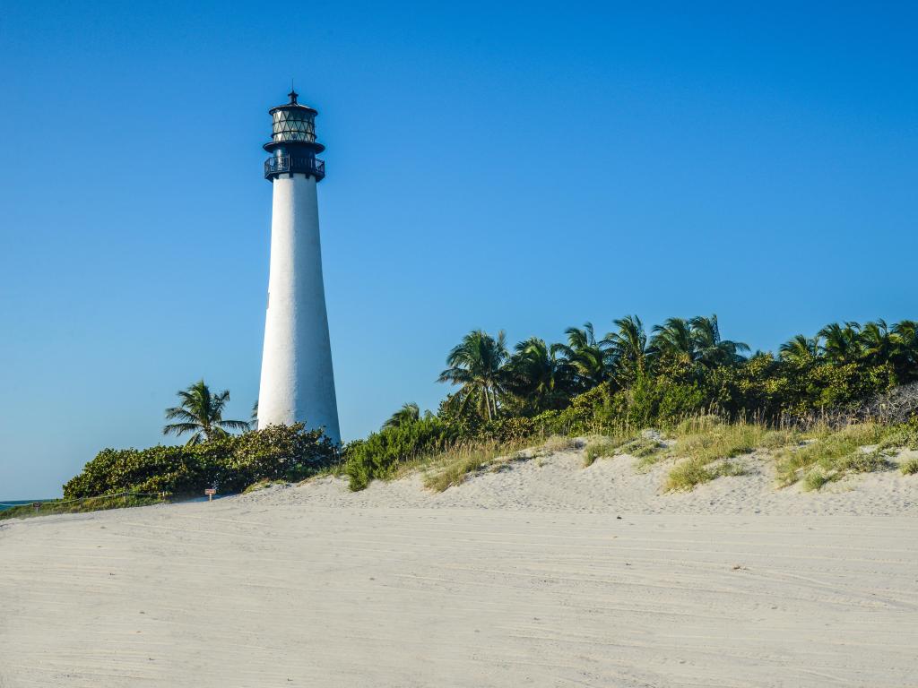 Lighthouse at Key West, Florida with the lighthouse in the distance and a white beach in the foreground under a blue sky.