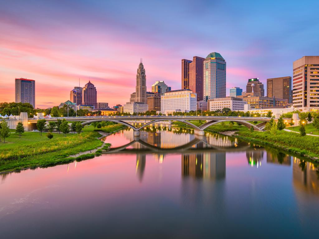 Columbus, Ohio, USA with the skyline on the river at dusk, the river in the foreground and bridge crossing over.