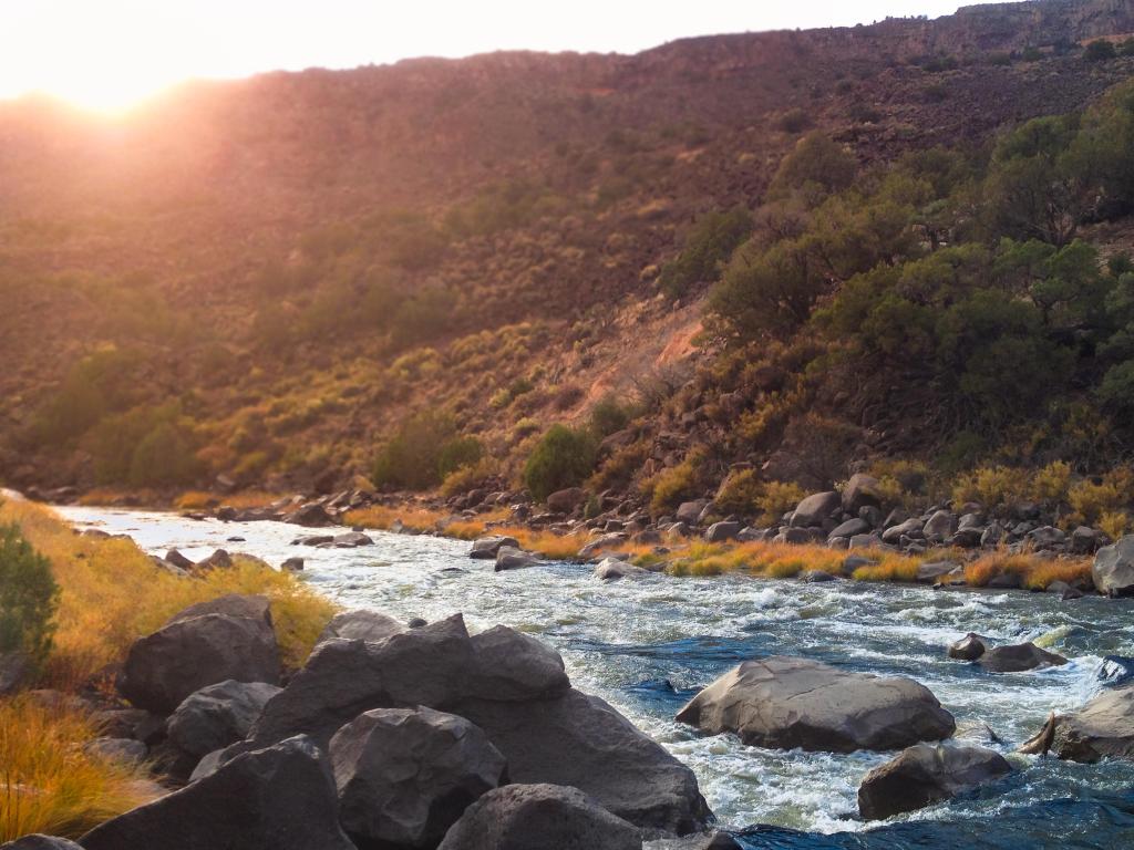 Rio Grande River, New Mexico, USA taken as a riverside view of the river as the sun dips is just about to dip below the gorge rim as the river babbles across rocks in the forefront.