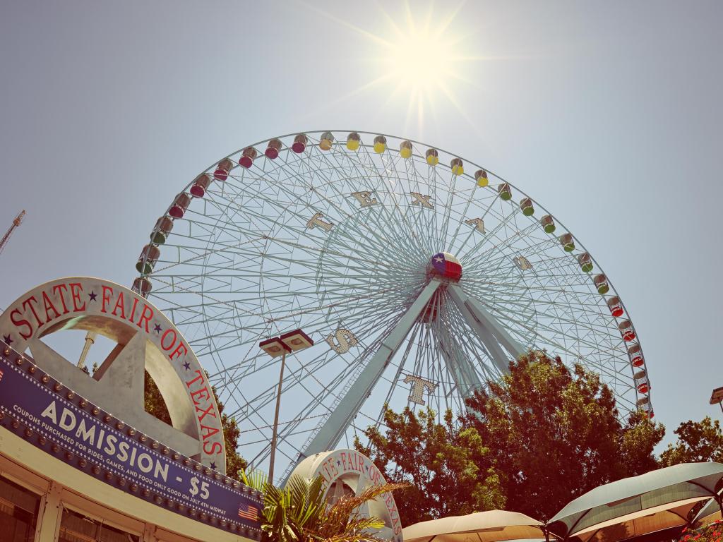 Large ferris wheel marked 'Texas' rises about the horizon